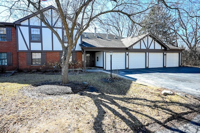 english style home featuring a shingled roof, brick siding, and driveway