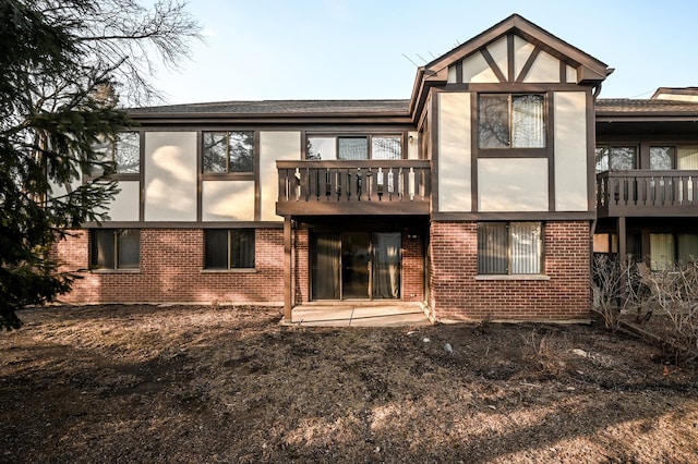 back of property with brick siding, a balcony, and stucco siding