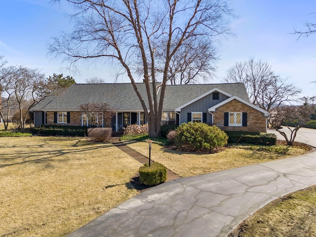 view of front facade with a front yard, driveway, board and batten siding, and roof with shingles