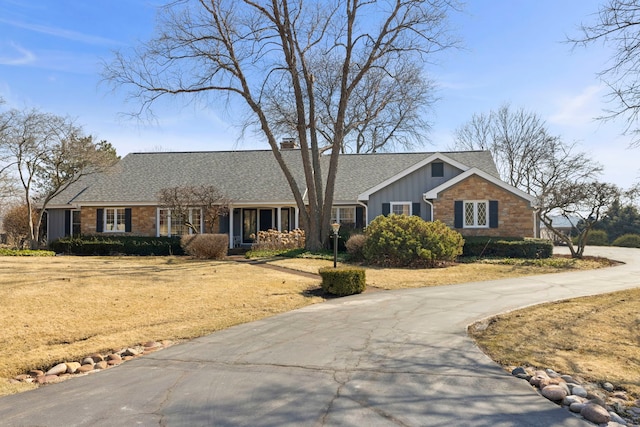 view of front of house featuring board and batten siding, a front lawn, roof with shingles, a chimney, and stone siding