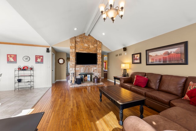 living room with hardwood / wood-style floors, visible vents, baseboards, lofted ceiling with beams, and a stone fireplace