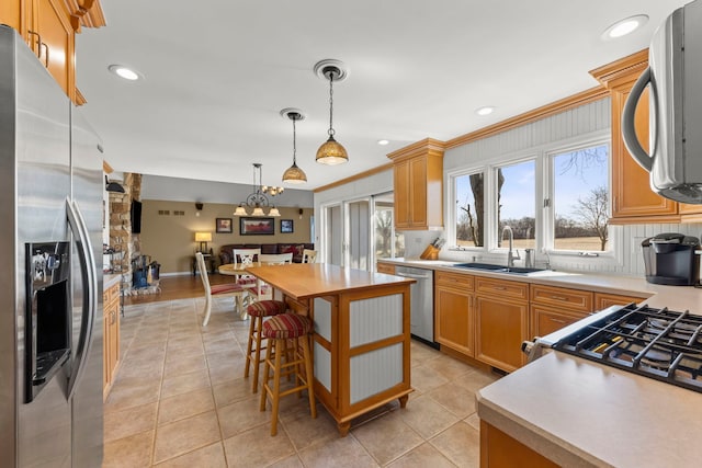 kitchen with ornamental molding, a sink, decorative light fixtures, appliances with stainless steel finishes, and light countertops