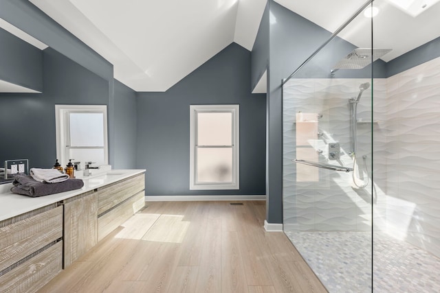 bathroom featuring wood finished floors, baseboards, walk in shower, vanity, and vaulted ceiling