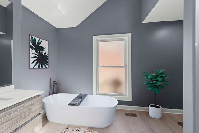 full bath with visible vents, baseboards, a freestanding bath, vaulted ceiling, and wood finished floors