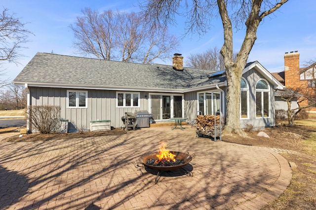 back of property featuring roof with shingles, an outdoor fire pit, a chimney, a patio area, and board and batten siding