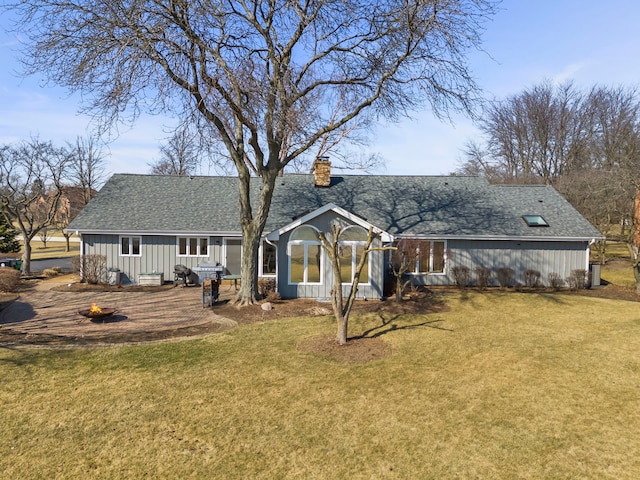 rear view of house featuring a lawn, a chimney, a fire pit, and roof with shingles