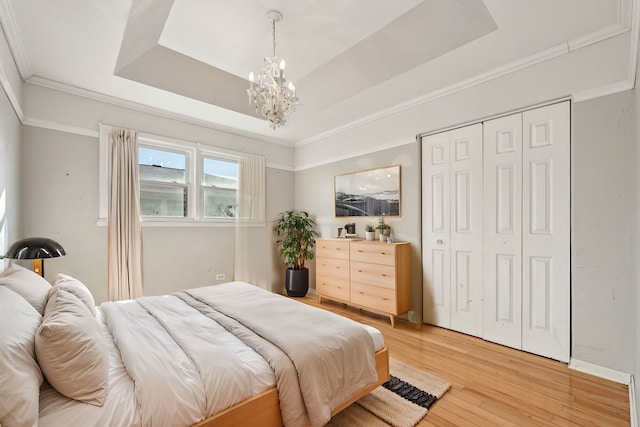 bedroom with a chandelier, wood finished floors, ornamental molding, a closet, and a raised ceiling