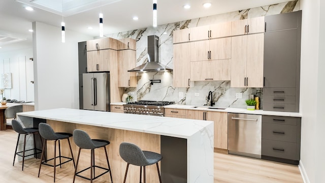 kitchen with premium appliances, a center island, a breakfast bar area, a sink, and wall chimney range hood