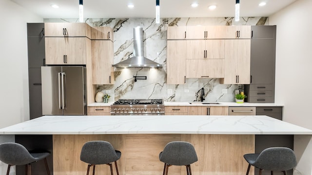 kitchen featuring high end appliances, light brown cabinetry, a kitchen island, a sink, and wall chimney exhaust hood