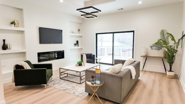 living room featuring visible vents, built in features, light wood-style flooring, and a glass covered fireplace