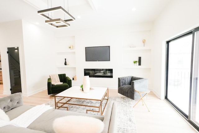 living area with built in features, recessed lighting, light wood-style flooring, a glass covered fireplace, and baseboards