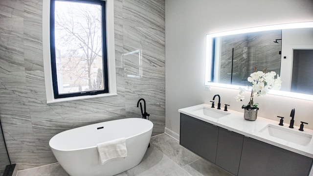 bathroom featuring marble finish floor, double vanity, a freestanding tub, and a sink