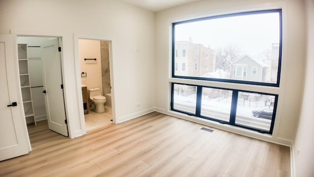 unfurnished bedroom featuring light wood-type flooring, visible vents, a spacious closet, and baseboards