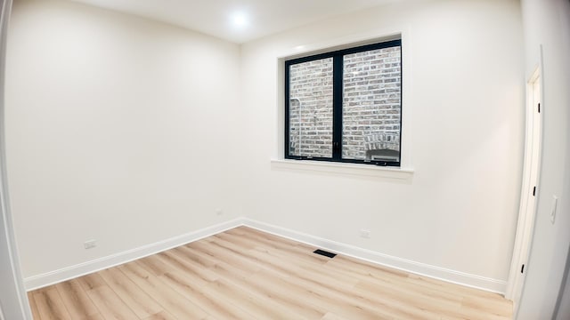 spare room featuring light wood finished floors, visible vents, and baseboards