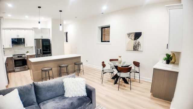 kitchen featuring light countertops, hanging light fixtures, appliances with stainless steel finishes, open floor plan, and white cabinetry