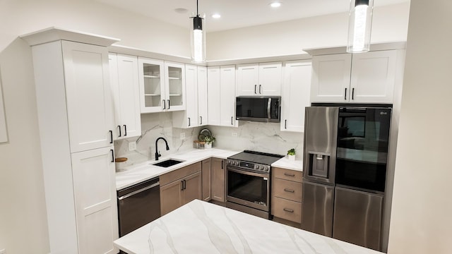 kitchen with light stone counters, pendant lighting, stainless steel appliances, glass insert cabinets, and white cabinetry