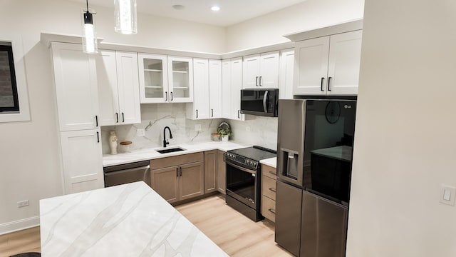 kitchen featuring decorative light fixtures, appliances with stainless steel finishes, glass insert cabinets, a sink, and light stone countertops