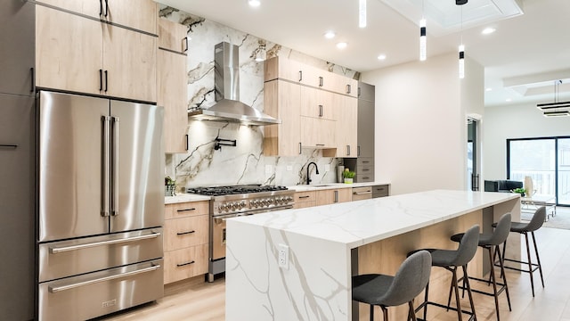 kitchen with wall chimney range hood, light brown cabinets, high quality appliances, and a center island