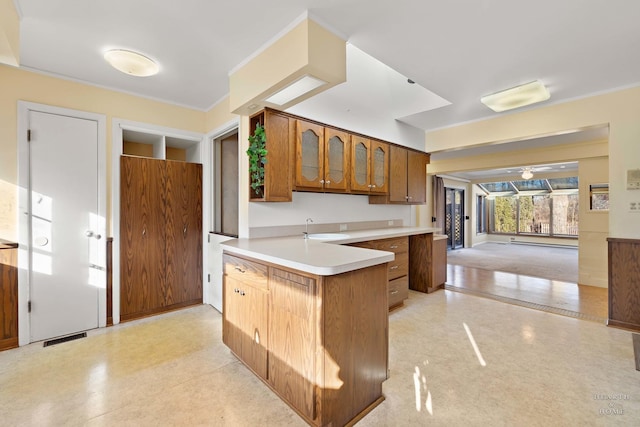 kitchen with a sink, visible vents, light countertops, brown cabinets, and glass insert cabinets