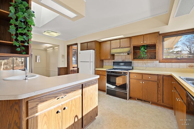 kitchen featuring light floors, gas range oven, light countertops, freestanding refrigerator, and under cabinet range hood