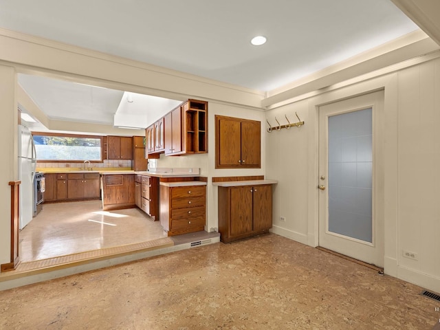 kitchen featuring brown cabinets, open shelves, light countertops, freestanding refrigerator, and a sink