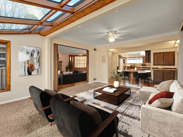 living room with ceiling fan, light colored carpet, a skylight, baseboards, and ornamental molding