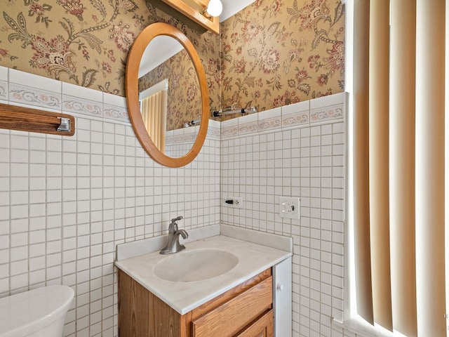 half bath with wainscoting, vanity, toilet, and wallpapered walls