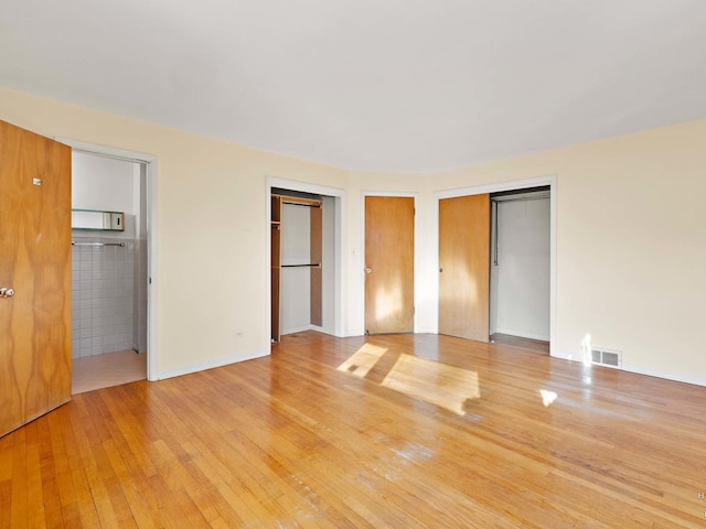 unfurnished bedroom with light wood-type flooring, connected bathroom, visible vents, and multiple closets