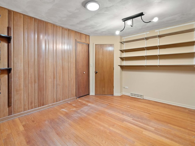 spare room with light wood-style flooring, wood walls, visible vents, and baseboards