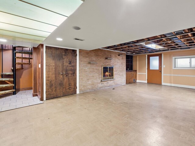 basement with light floors, visible vents, a brick fireplace, brick wall, and stairs