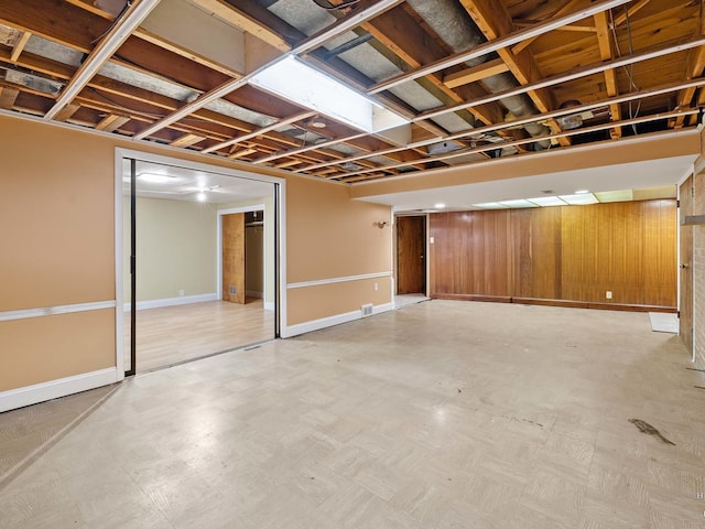 finished below grade area featuring light floors, wooden walls, and baseboards