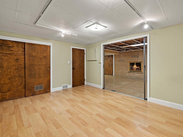 below grade area featuring a brick fireplace, visible vents, and light wood-style flooring