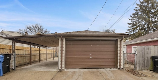 detached garage featuring a carport, concrete driveway, and fence