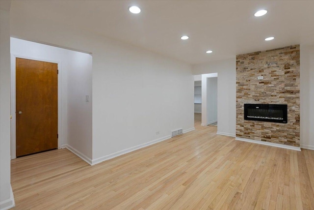 unfurnished living room with a stone fireplace, recessed lighting, wood finished floors, and visible vents