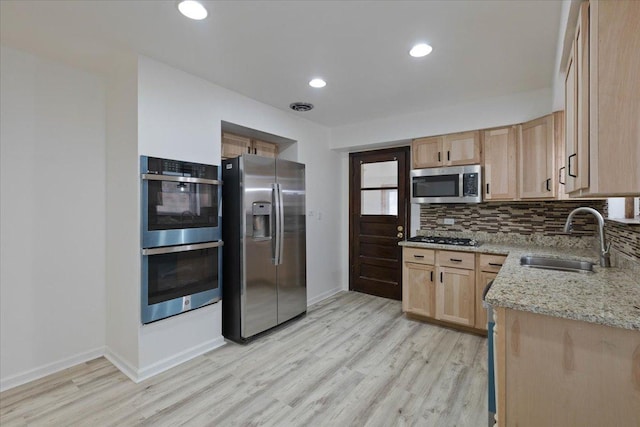 kitchen with tasteful backsplash, light brown cabinets, light stone counters, stainless steel appliances, and a sink