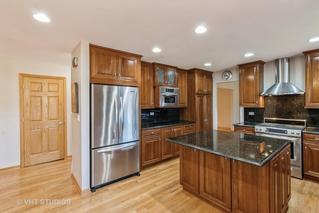 kitchen featuring light wood-style flooring, a center island, appliances with stainless steel finishes, wall chimney range hood, and brown cabinets