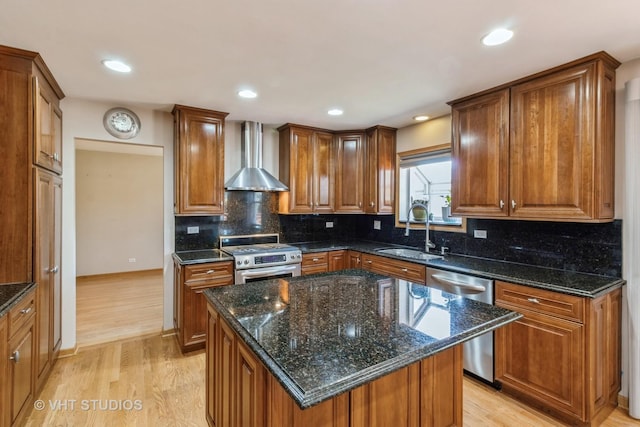 kitchen with a kitchen island, appliances with stainless steel finishes, brown cabinets, wall chimney range hood, and a sink