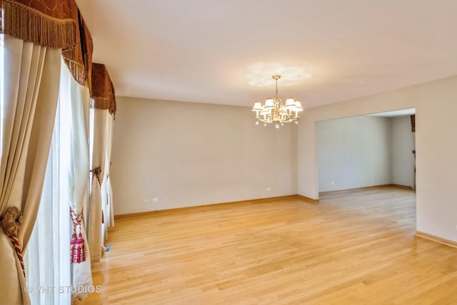 empty room with a chandelier, light wood-type flooring, and baseboards