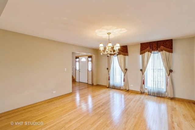 spare room with a chandelier, light wood finished floors, and baseboards