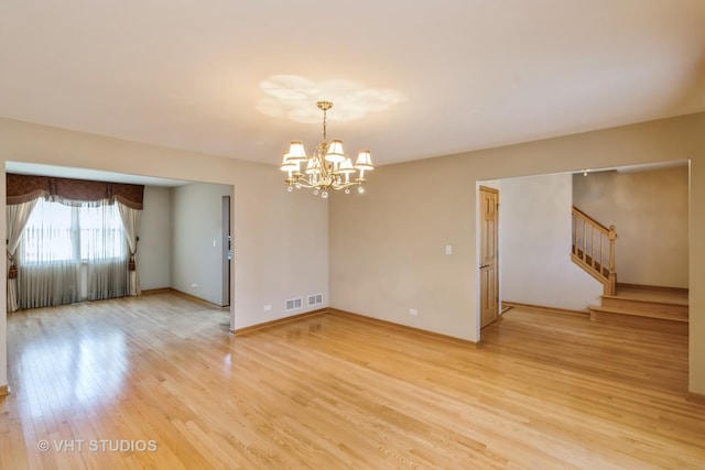 spare room featuring visible vents, baseboards, stairway, light wood-type flooring, and a chandelier