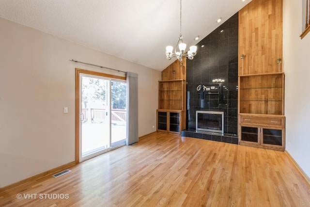 unfurnished living room with a tile fireplace, visible vents, a notable chandelier, and wood finished floors