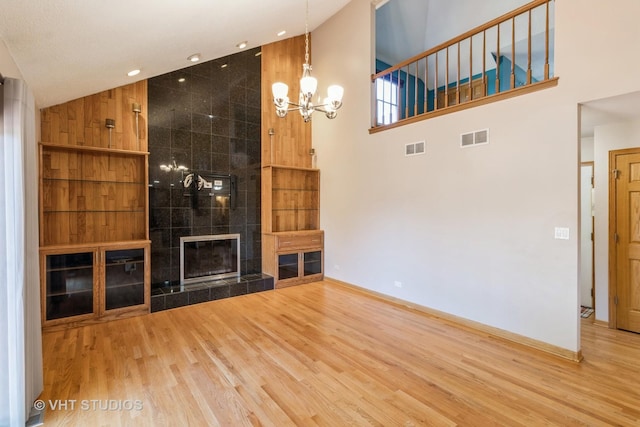 unfurnished living room featuring visible vents, a notable chandelier, a tiled fireplace, and wood finished floors