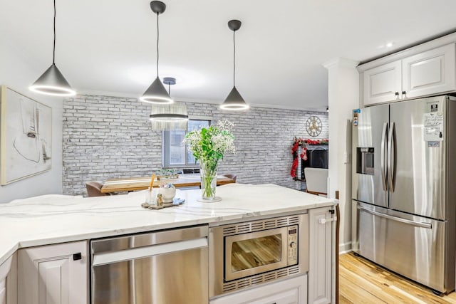 kitchen featuring stainless steel appliances, pendant lighting, crown molding, and light stone counters