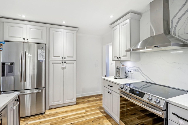 kitchen with wall chimney range hood, light stone countertops, appliances with stainless steel finishes, and white cabinetry