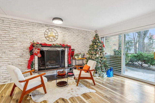 living area featuring ornamental molding, a fireplace, brick wall, and wood finished floors