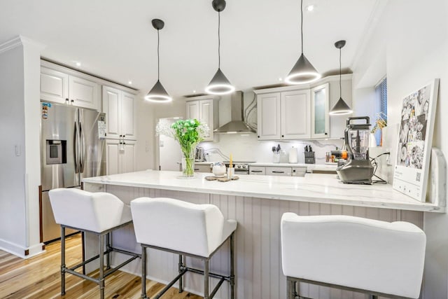 kitchen featuring white cabinets, wall chimney range hood, stainless steel fridge, and pendant lighting