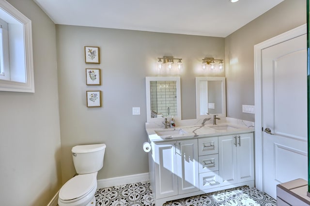 bathroom with toilet, double vanity, baseboards, and a sink