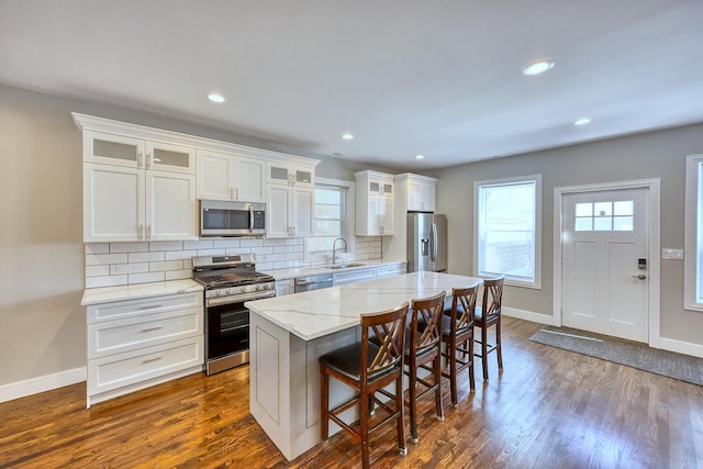 kitchen featuring white cabinets, glass insert cabinets, appliances with stainless steel finishes, a center island, and a sink