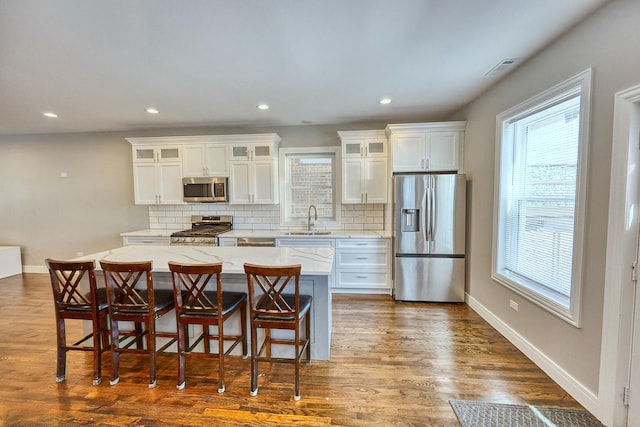 kitchen featuring white cabinets, a kitchen island, glass insert cabinets, appliances with stainless steel finishes, and a sink