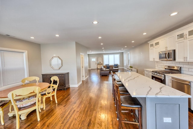 kitchen featuring a kitchen island, white cabinetry, appliances with stainless steel finishes, light stone countertops, and glass insert cabinets